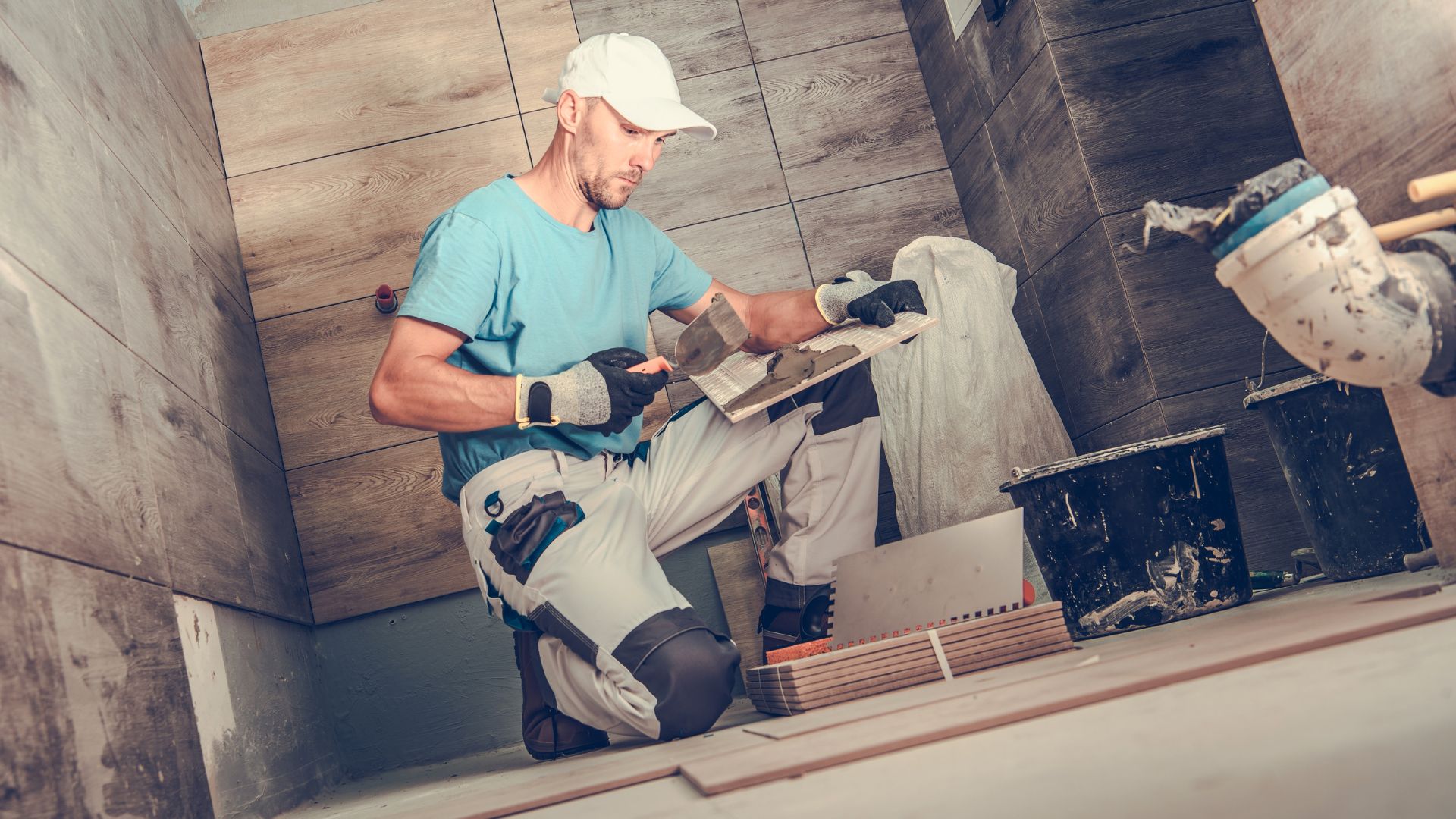 A worker kneels in the middle of floor, surrounded by his tools, working on a bathroom remodel.