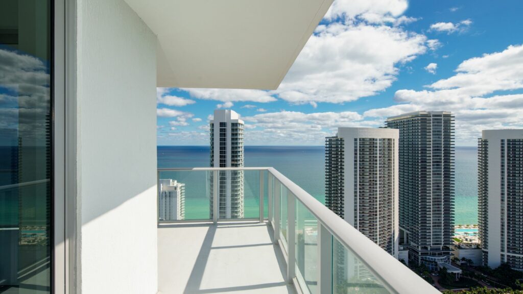 A view off the balcony of a luxury condo, overlooking a cityscape and the sea.