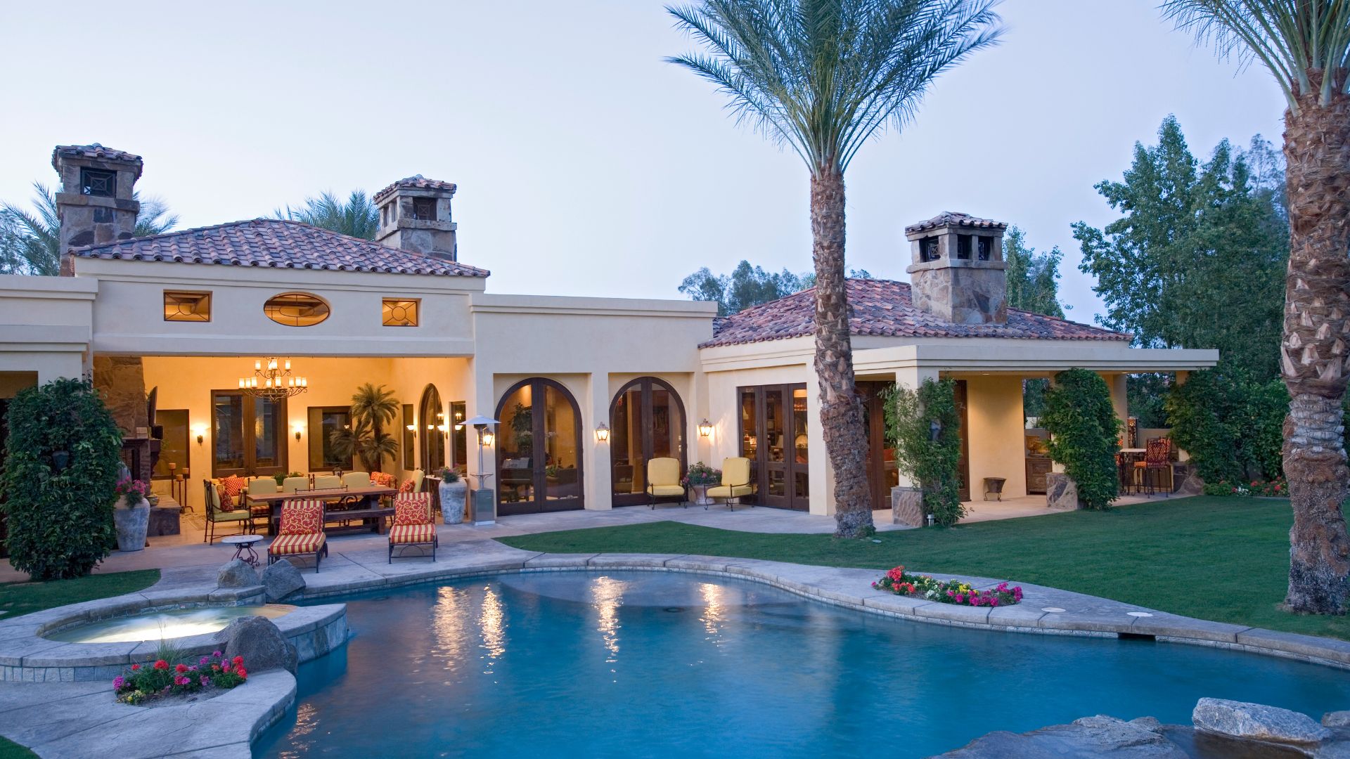 A beautiful luxury home surrounded by palm trees and featuring a pool.